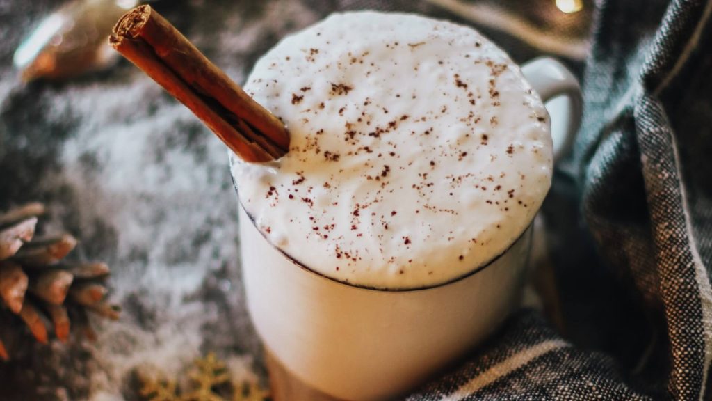 A cup of eggnog with a cinnamon stick and nutmeg on top