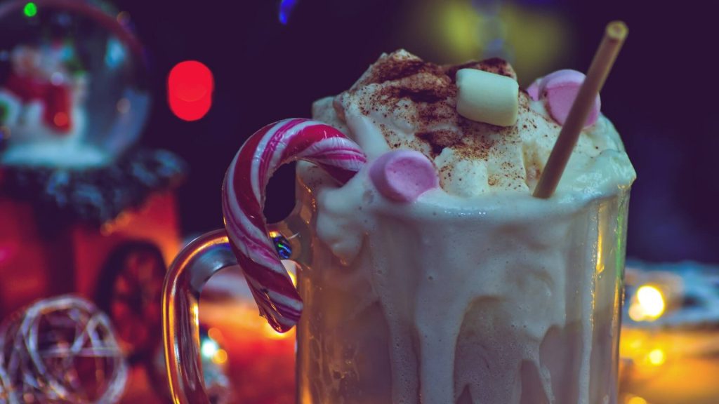 A cup of hot chocolate with marshmallows, a candy cane and whipped cream